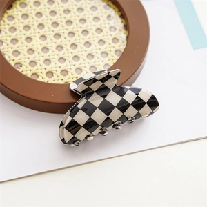 Close-up of black and white checkered hair claw clip on a woven tray with natural shadows