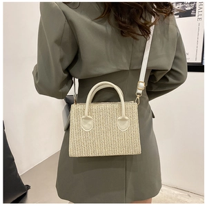 Detail of beige woven crossbody bag with leather handles shown on a model