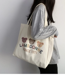 Side view of large off-white canvas tote bag with bear print and Lambdonne graphics