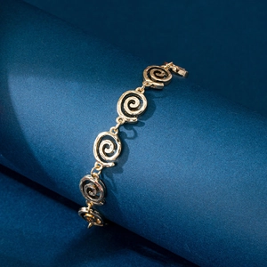 Detailed close-up of golden spiral metal link bracelet on a blue cylindrical stand