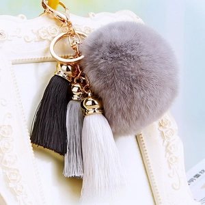 Detail of grey fluffy faux fur pom-pom with black, grey, and white silk tassels on gold ring