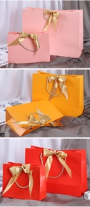 Detailed view of colorful paper gift bags featuring satin bows and braided handles