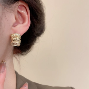 Close-up of golden wrinkled texture stud earrings worn on a model ear for a luxury look
