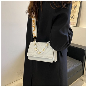 Detail of white quilted crossbody bag with wide patterned strap and gold chain accent