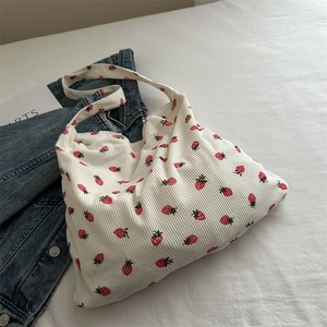 White corduroy tote bag with strawberry print on a bed in a cozy home setting