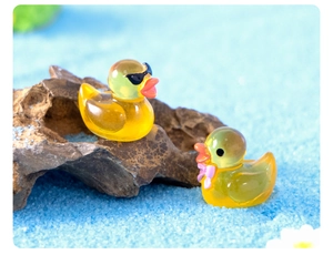 Macro shot of mini resin ducks with sunglasses and pink bow on blue sand landscape