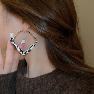 Detail of large geometric leopard print earrings with gold plating on model