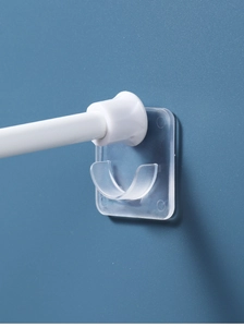 Détail de supports adhésifs transparents fixant une barre de rideau blanche sur un mur