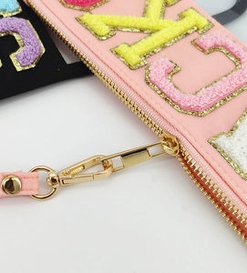 Detail of pink travel bag with colorful chenille PACK lettering and gold zipper