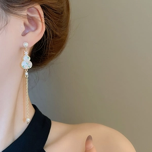 Detail of elegant gold tassel earrings with pearl and gourd pendant on female model