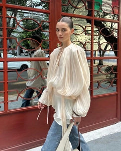 Outdoor shot of light beige pleated puff sleeve blouse with tie neck and sheer fabric detail
