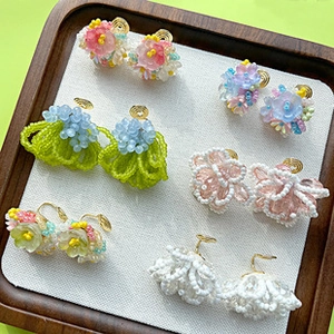 Macro detail of handmade beaded flower earrings in various pastel colors on a tray