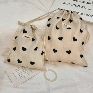 Detail view of two beige drawstring bags with black heart prints and wrinkled texture