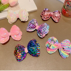 Flat lay of colorful sequin bow hair clips for girls on a wooden desk with flowers