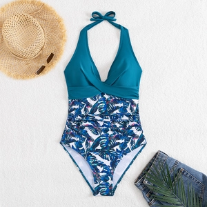 Flat lay of teal halter one-piece swimsuit with tropical leaf print and beach accessories