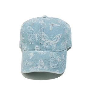 Detail of white butterfly embroidery on light blue denim fabric of the baseball cap