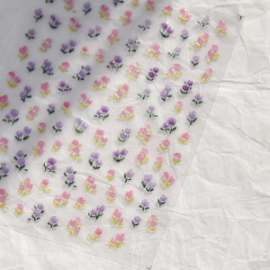 Macro shot of tulip nail stickers in purple and pink with green leaves on transparent film