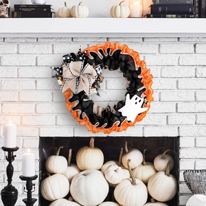 Halloween ghost wreath with orange and black burlap mesh and a large bow on white brick wall