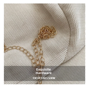 Detailed macro view of a glossy gold metal chain strap on textured beige corduroy fabric