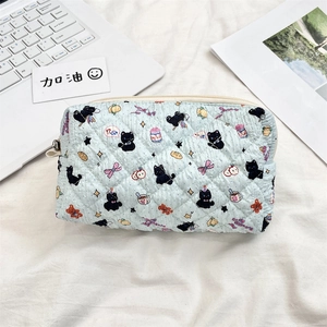 Detail of light blue quilted pouch with black cat patterns on a soft white surface