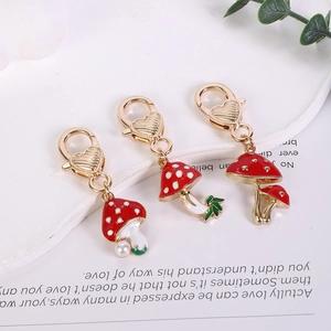 Detail view of red enamel mushroom keychains with gold heart clips on a white tray