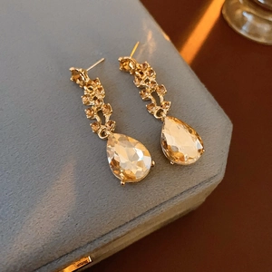 Macro view of gold teardrop earrings with crystals on a grey luxury jewelry box