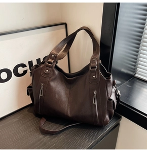 Detail view of large dark brown tote bag with decorative zippers and side pockets