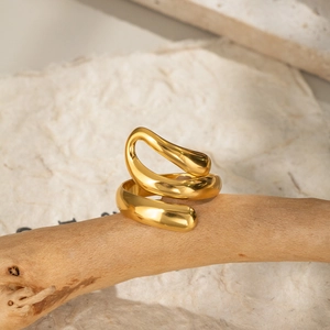 Macro detail of gold fluid wave ring showing mirrored texture on natural wood branch