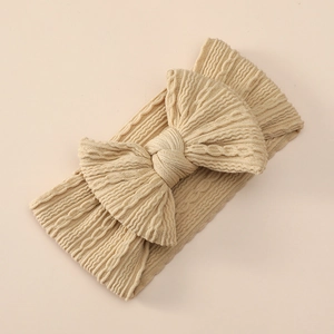 Macro shot of knitted beige nylon baby headband with textured jacquard bow detail