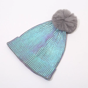 Detail of holographic purple knitted beanie with a large fluffy grey faux fur pompom
