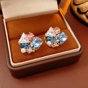 Detailed shot of gold earrings with blue, pink, and white gemstones in a velvet jewelry box