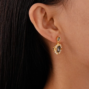 Close-up of vintage gold earrings with black oval gemstone and pearl halo on a model