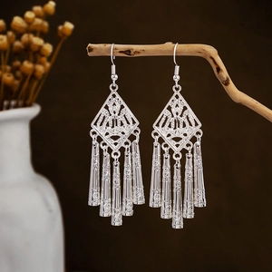 Close-up of ethnic silver leaf tassel earrings hanging on wood with bohemian hollow design