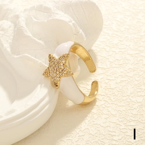 Detail of adjustable gold star ring with white enamel finish and shimmering zircons