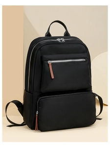 Detailed close-up of a black nylon backpack featuring silver zippers and brown leather pulls