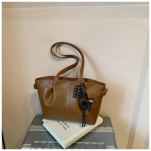 Detail of a brown pleated tote bag with a cute black cat charm on a metallic box