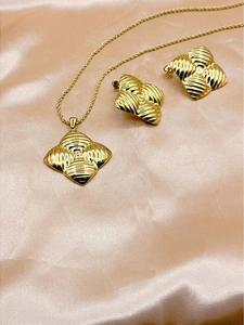 Detailed view of golden textured clover necklace and earrings on champagne silk