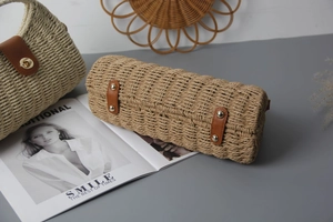 Detail of woven straw bag base with brown leather straps and four gold metal feet