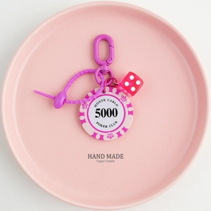 Detail of pink poker chip 5000 and red dice charm keychain with purple clip