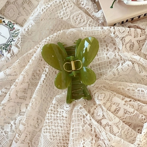 Détail de la pince à cheveux papillon vert foncé avec ressort doré sur fond de dentelle