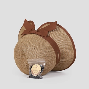 Detailed view of sun hat with brown bow, UV protection tag and included hair tie