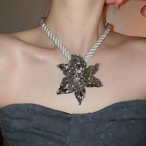 Close-up of a bold silver metal flower pendant necklace with rope chain on a model