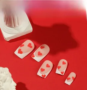 Detailed macro view of matte French nails with red heart patterns and white edges