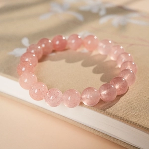 Pink strawberry quartz beaded bracelet placed on a beige book in a cozy setting