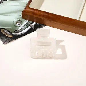 Close-up of a square pearlescent white hair claw clip displayed on a wooden tray