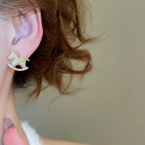 Detailed close-up of a golden rocking horse stud earring with sparkling cubic zirconia