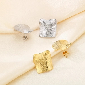 Detail shot of square textured gold and silver earrings on light yellow satin fabric