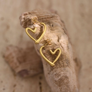 Detail showing high-polish heart-shaped gold earrings on textured stone surface