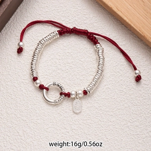 Detail view of red braided bracelet with silver beads and carved prosperity charm
