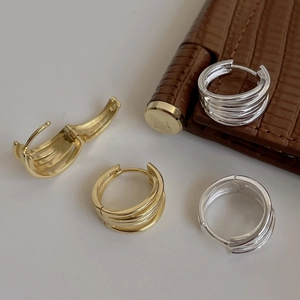 Detail of layered gold and silver hoop earrings on a minimalist white and brown leather base